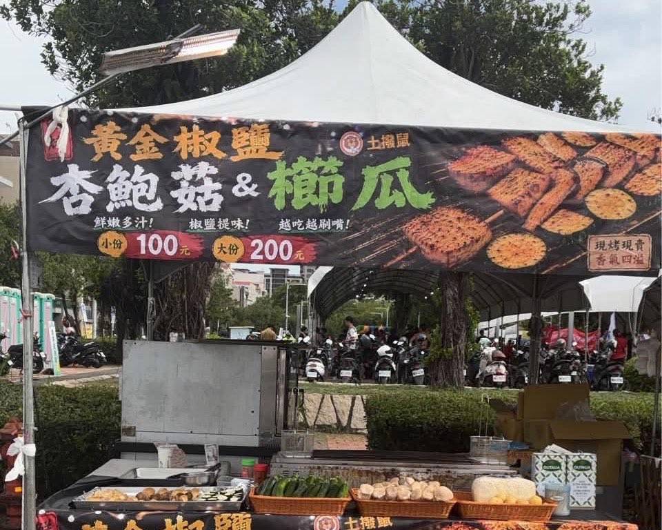 土撥鼠的實際攤位：白色帳篷下掛著黃金椒鹽杏鮑菇與櫛瓜的黑色帆布招牌，寫著小份 100 元、大份 200 元